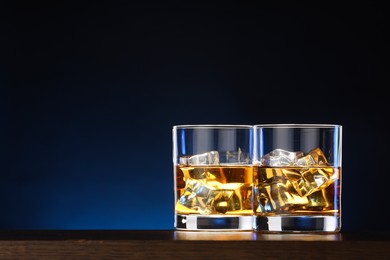 Whiskey with ice cubes in glasses on table against dark background. Space for text
