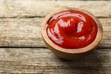 Photo of Tasty ketchup in bowl on wooden table, space for text. Tomato sauce