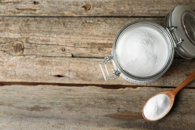 Photo of Baking soda in jar and spoon on wooden table, top view. Space for text