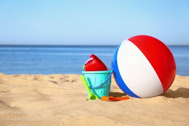 Photo of Set of plastic beach toys and colorful ball on sand near sea. Space for text