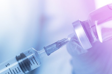 Doctor filling syringe with medication from vial, closeup. Color toned