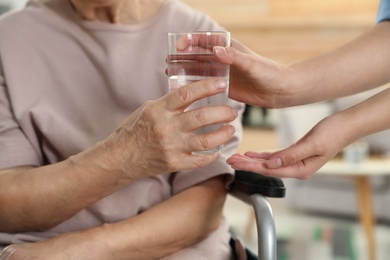 Photo of Nurse giving glass of water to elderly woman indoors, closeup. Assisting senior people