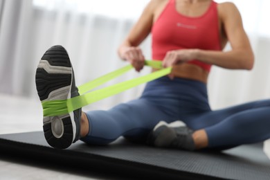 Photo of Woman doing exercise with fitness elastic band on mat indoors, closeup