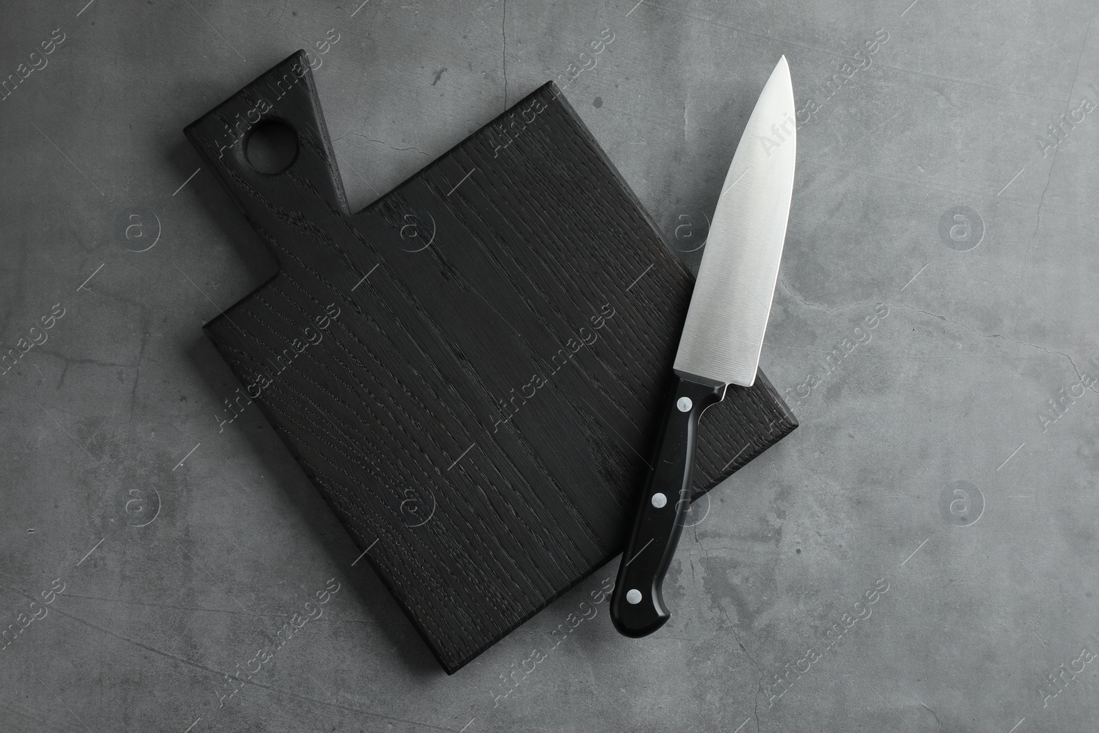 Photo of Knife and black wooden board on grey textured table, top view