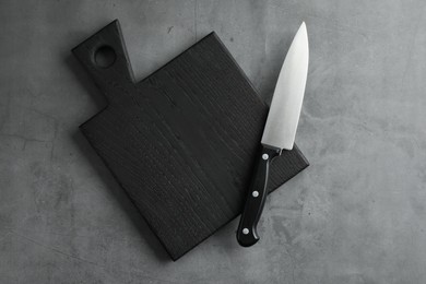 Photo of Knife and black wooden board on grey textured table, top view