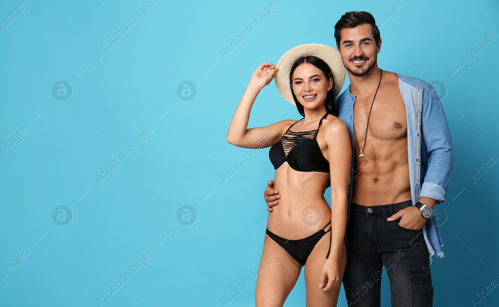 Photo of Beautiful young woman in stylish bikini and man on light blue background. Space for text