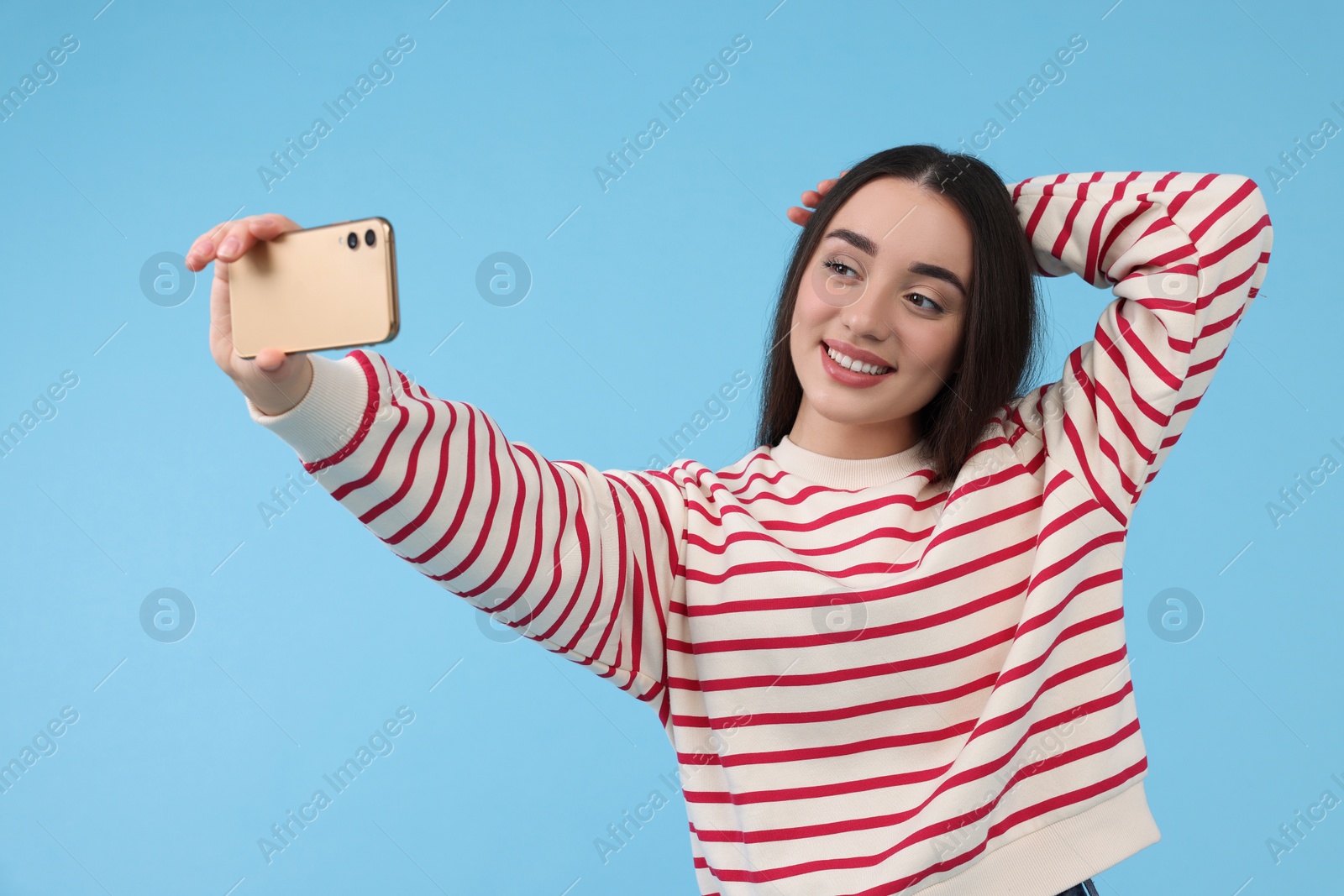 Photo of Smiling young woman taking selfie with smartphone on light blue background