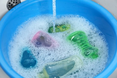 Photo of Light blue basin with baby bottles under stream of water in sink, closeup