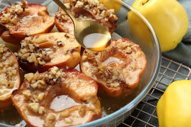 Photo of Pouring tasty honey onto baked quinces in bowl on table, closeup