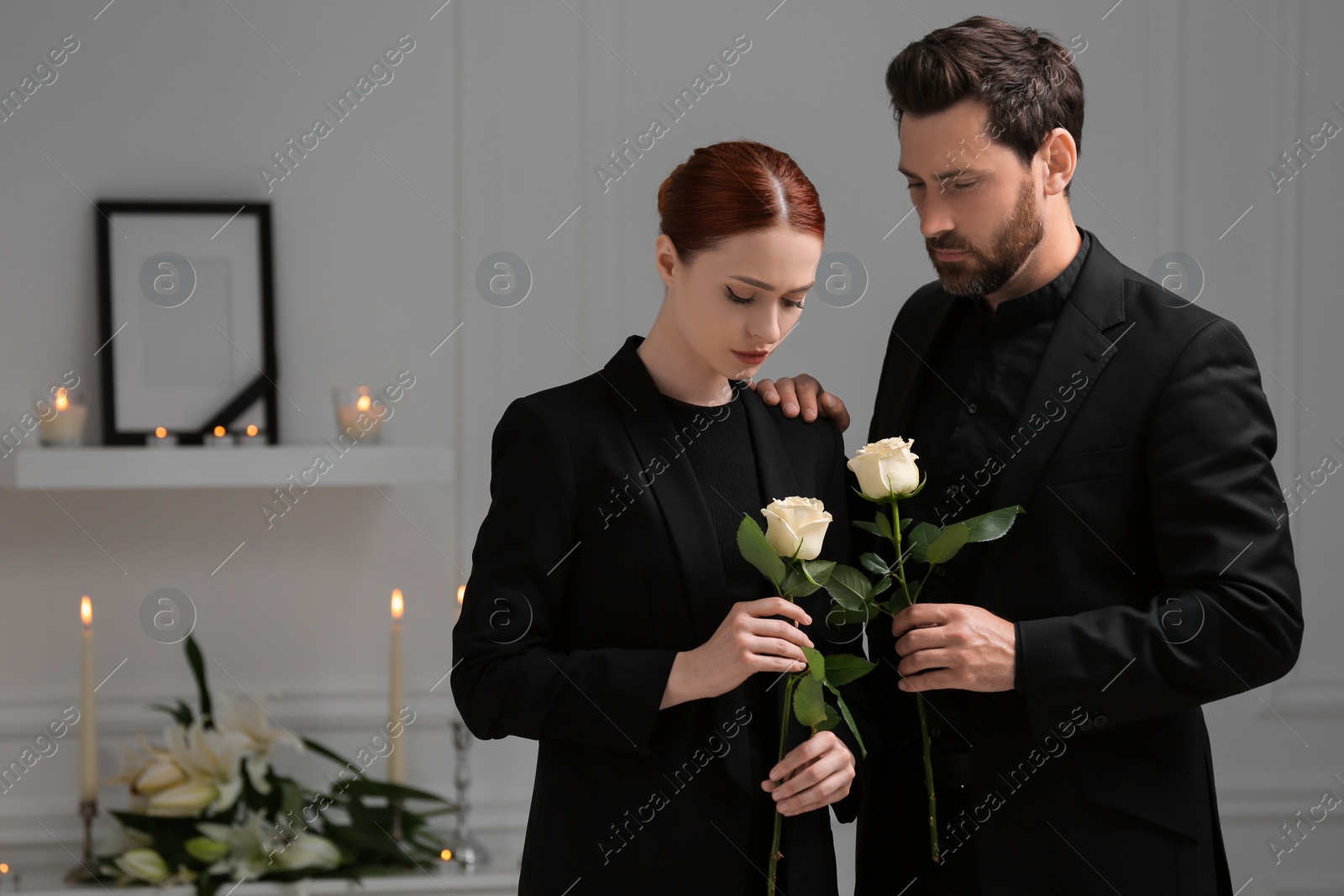 Photo of Sad couple with white roses mourning indoors. Funeral ceremony