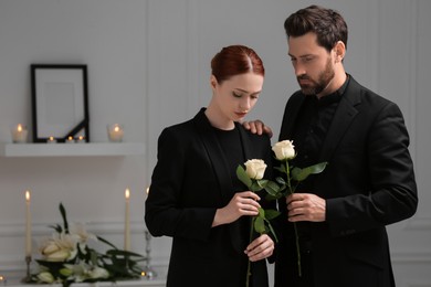Sad couple with white roses mourning indoors. Funeral ceremony
