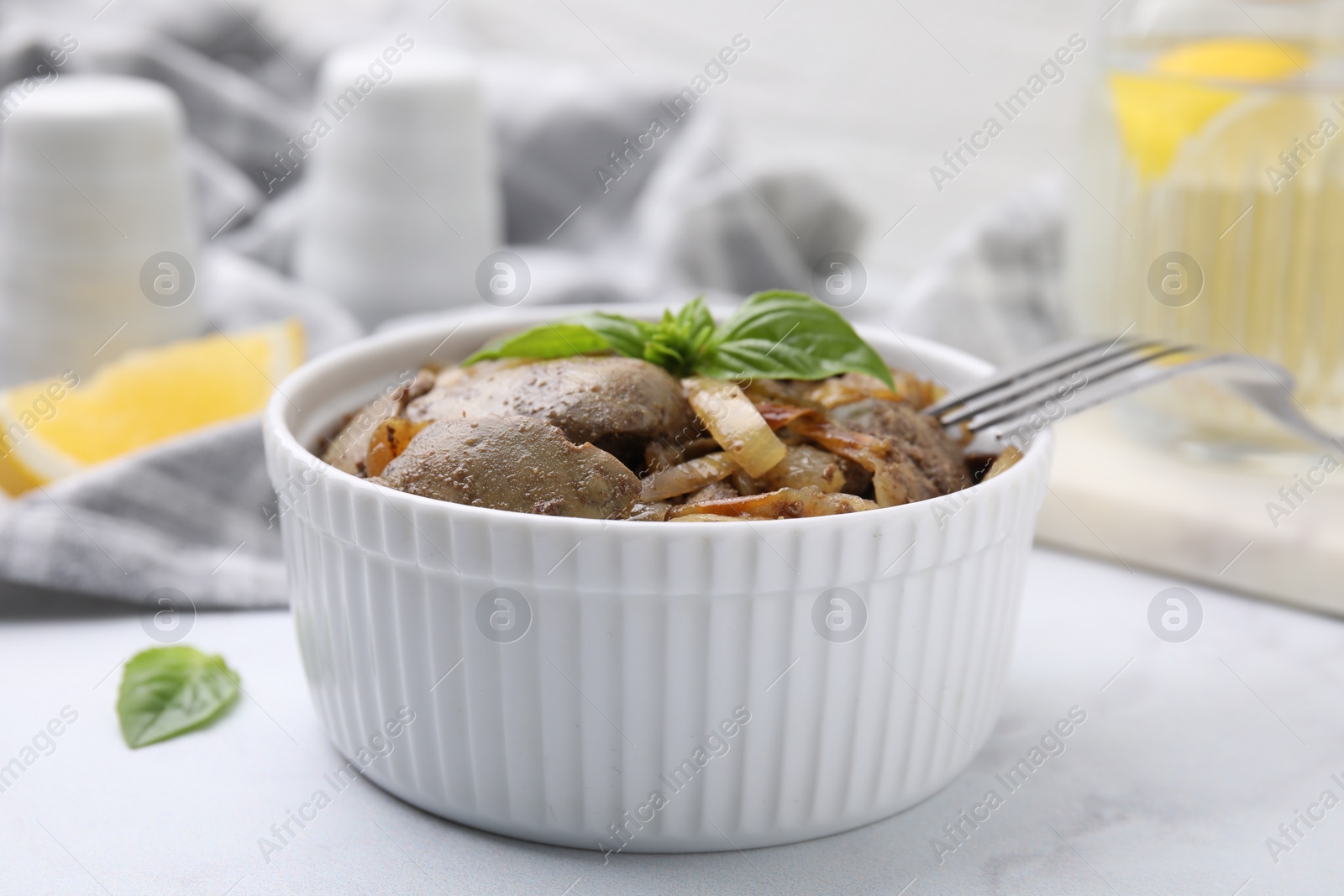 Photo of Delicious fried chicken liver with onion and basil in bowl on white table, closeup