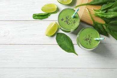 Photo of Glasses of healthy green smoothie with fresh spinach on white wooden table, flat lay. Space for text