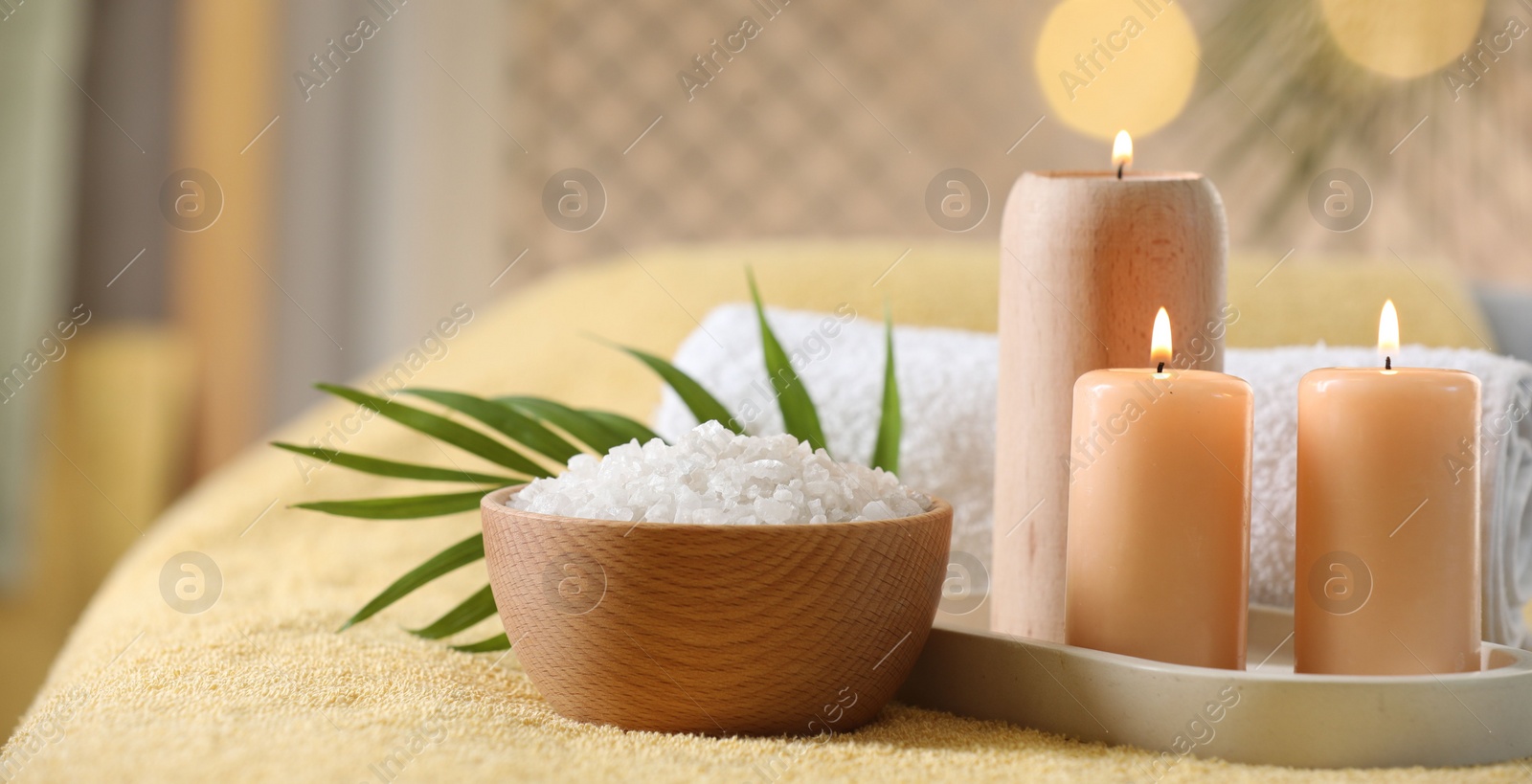 Photo of Spa composition. Burning candles, sea salt and towel on soft yellow surface, space for text