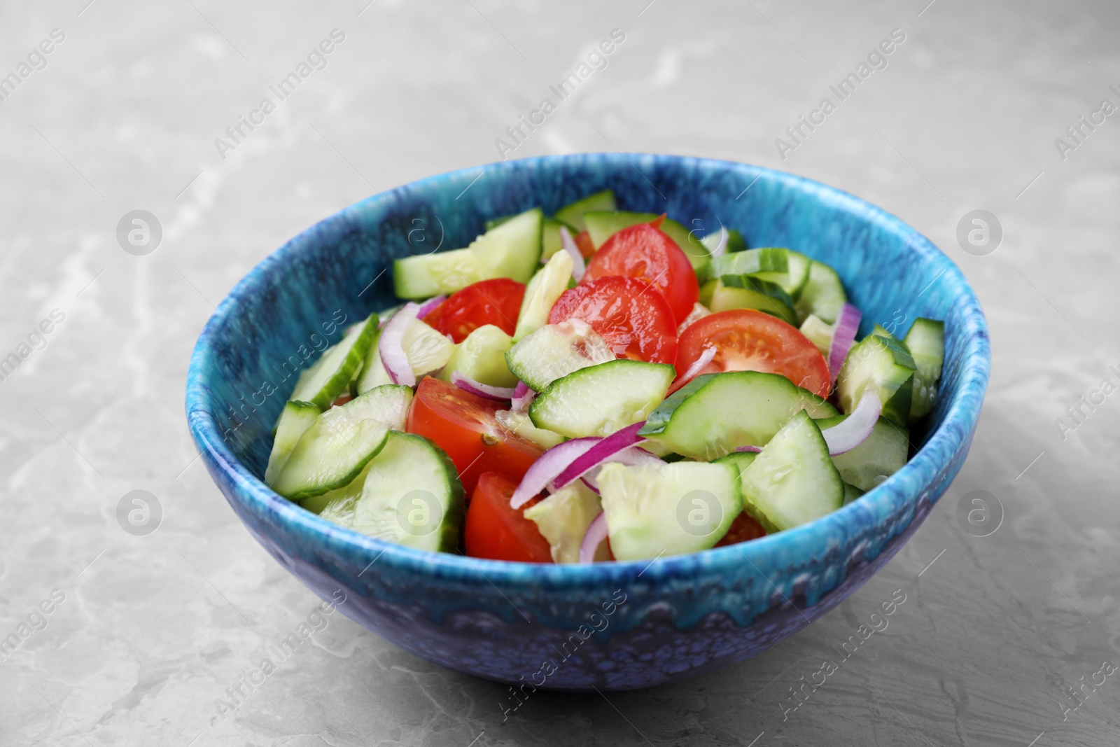 Photo of Bowl of vegetarian salad with cucumber, tomato and onion on table