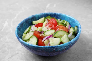 Bowl of vegetarian salad with cucumber, tomato and onion on table