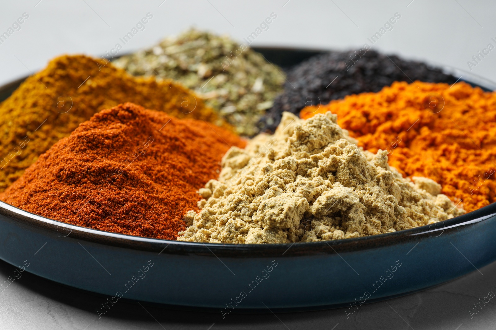 Photo of Plate with different spices on light grey table, closeup