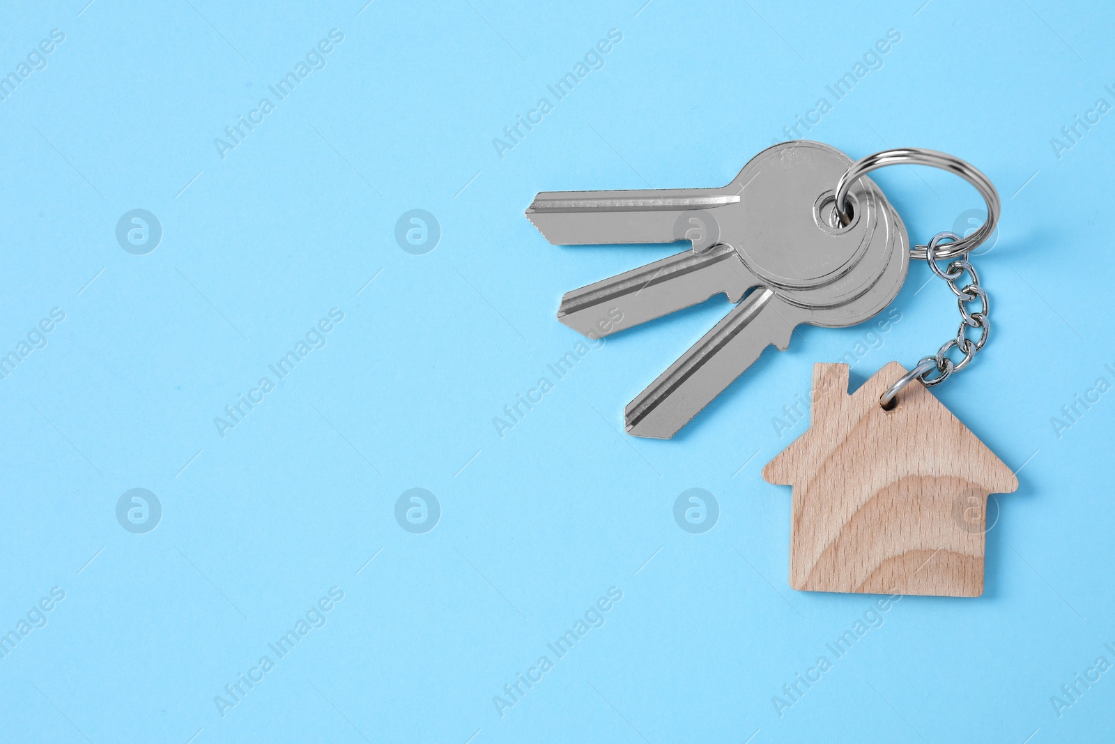 Photo of Keys with keychain in shape of house on light blue background, top view. Space for text
