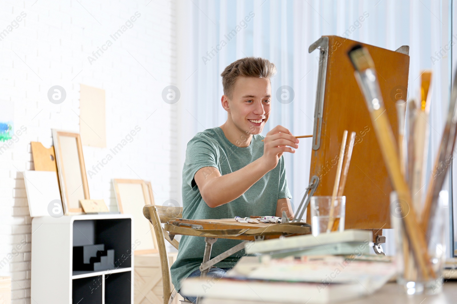 Photo of Teenage boy painting on easel in workshop, space for text. Hobby club