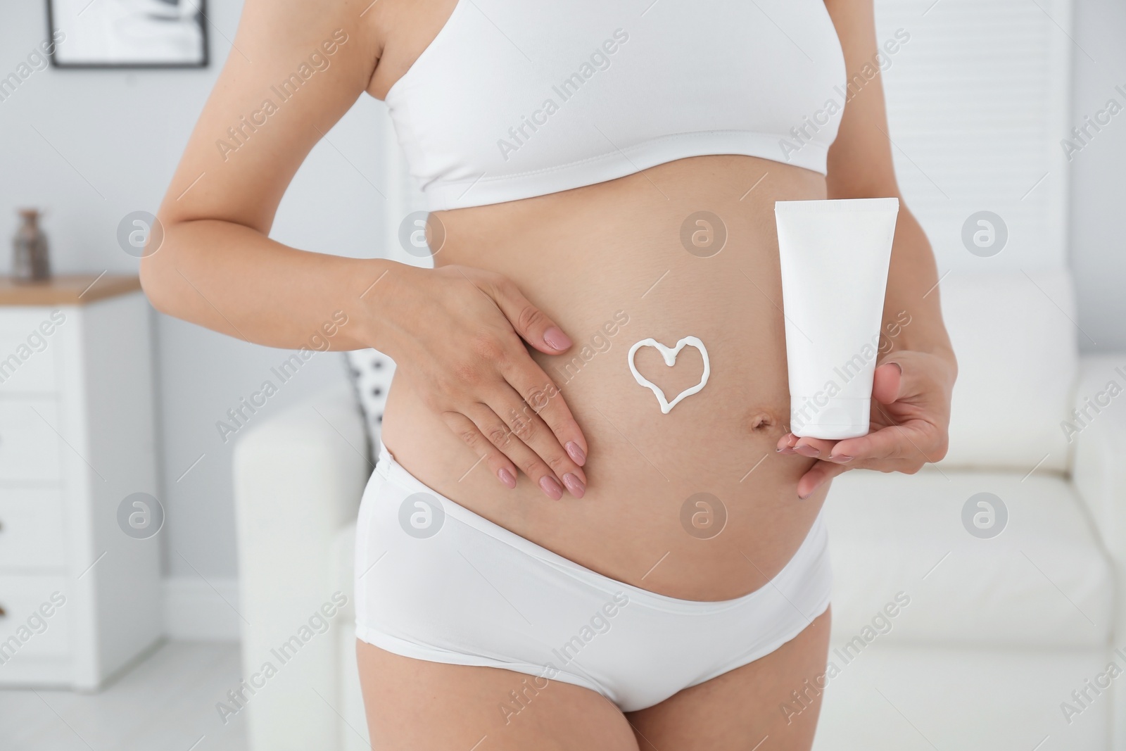 Photo of Heart painted with body cream on pregnant woman's belly at home, closeup