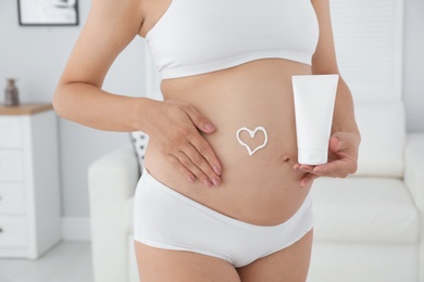 Heart painted with body cream on pregnant woman's belly at home, closeup