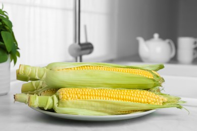 Tasty sweet corn cobs on white countertop in kitchen