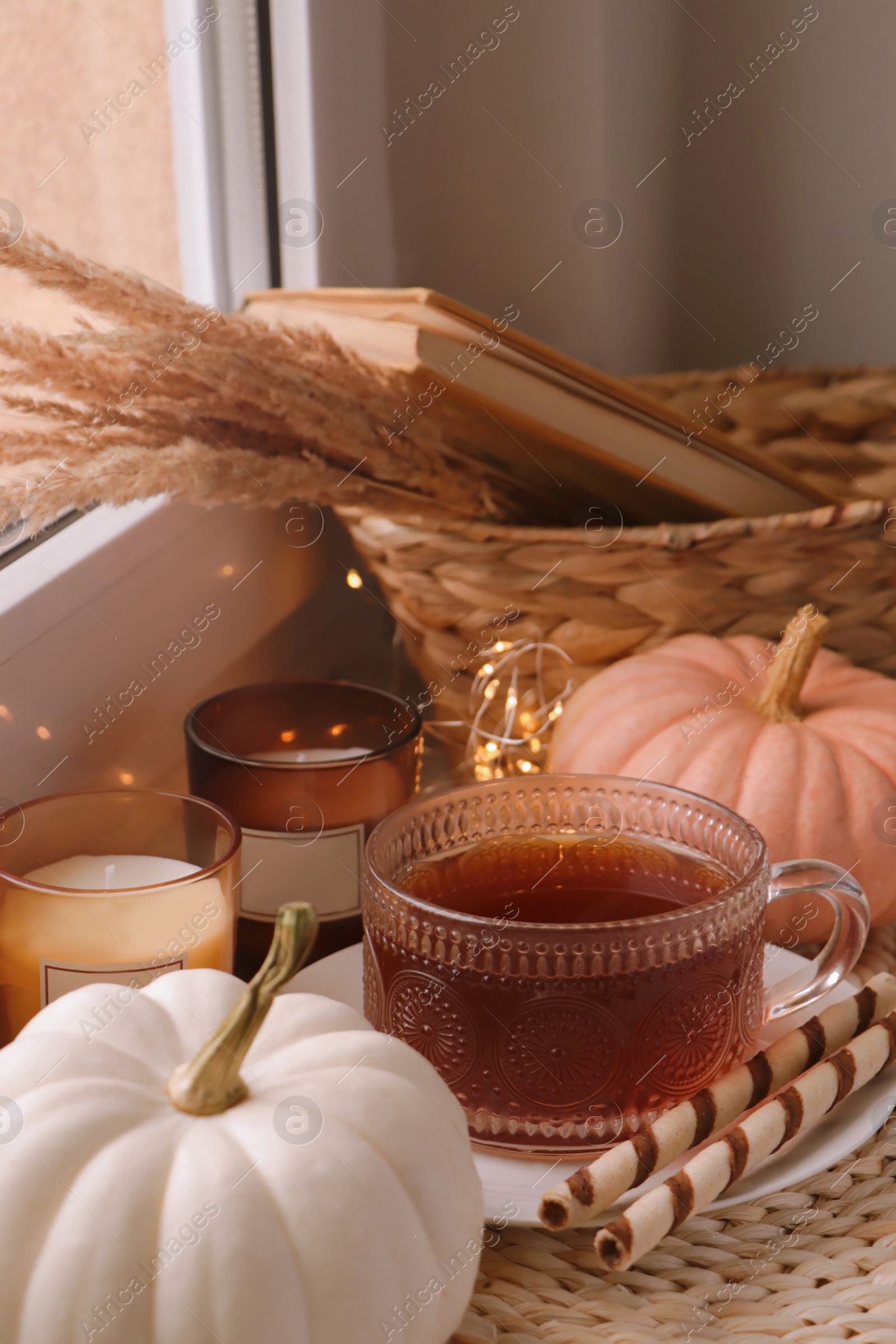 Photo of Cup of hot drink, cookies, candles and pumpkins on window sill indoors