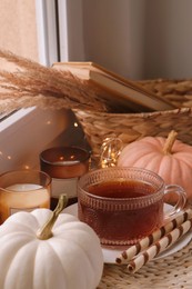 Photo of Cup of hot drink, cookies, candles and pumpkins on window sill indoors