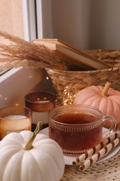 Cup of hot drink, cookies, candles and pumpkins on window sill indoors