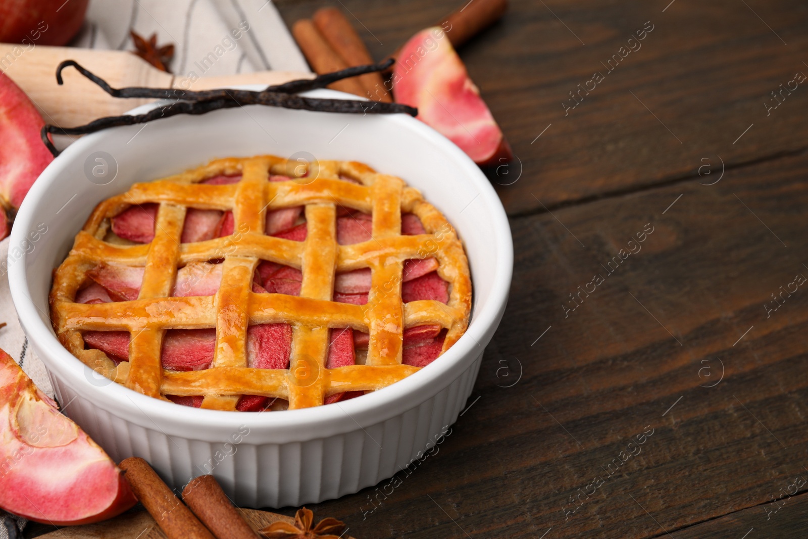 Photo of Baking dish with tasty apple pie and spices on wooden table. Space for text