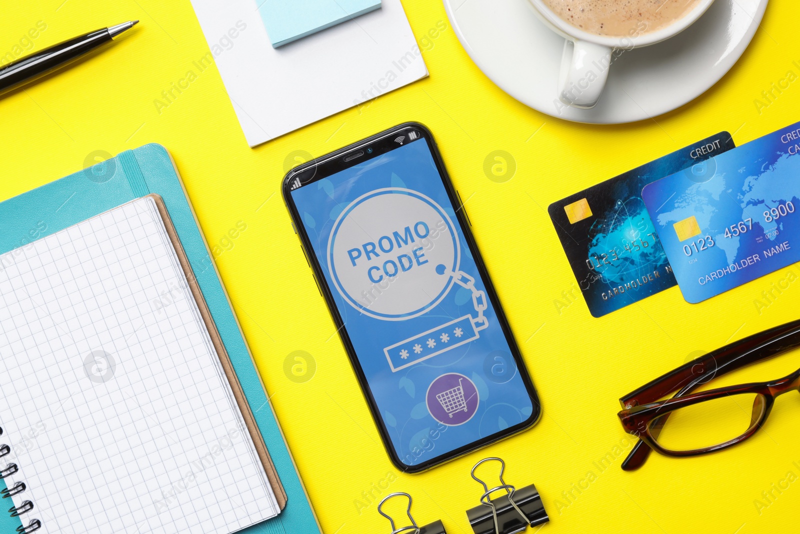 Photo of Flat lay composition of smartphone with activated promo code, credit cards and stationery on yellow table