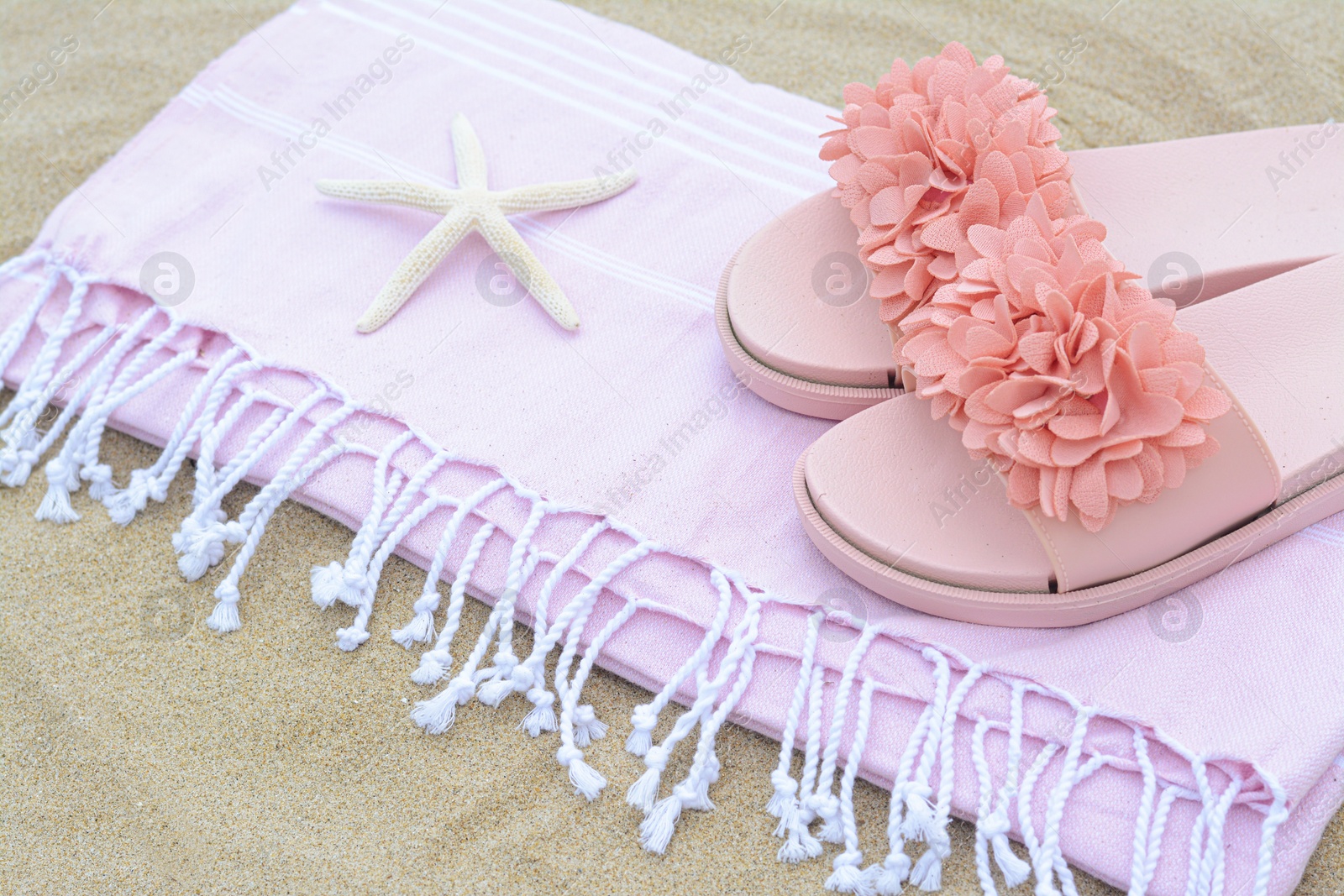 Photo of Blanket with stylish slippers and starfish on sand outdoors, closeup. Beach accessories