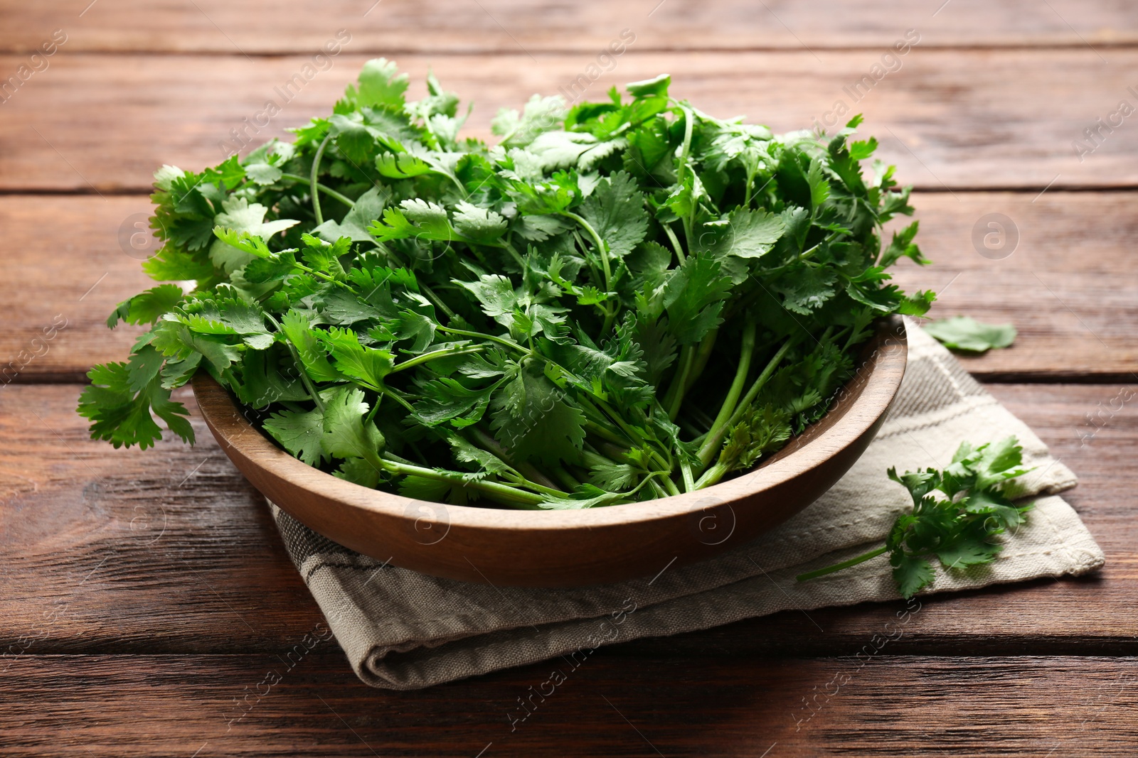 Photo of Fresh coriander in bowl on wooden table, closeup