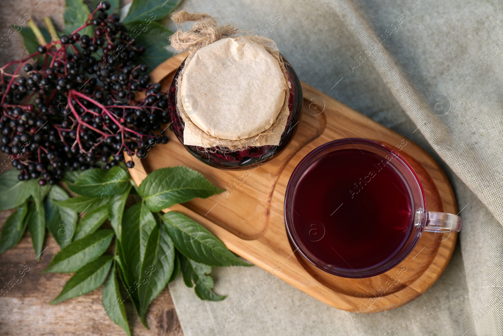 Photo of Elderberry jam, glass cup of tea and Sambucus berries on table, flat lay
