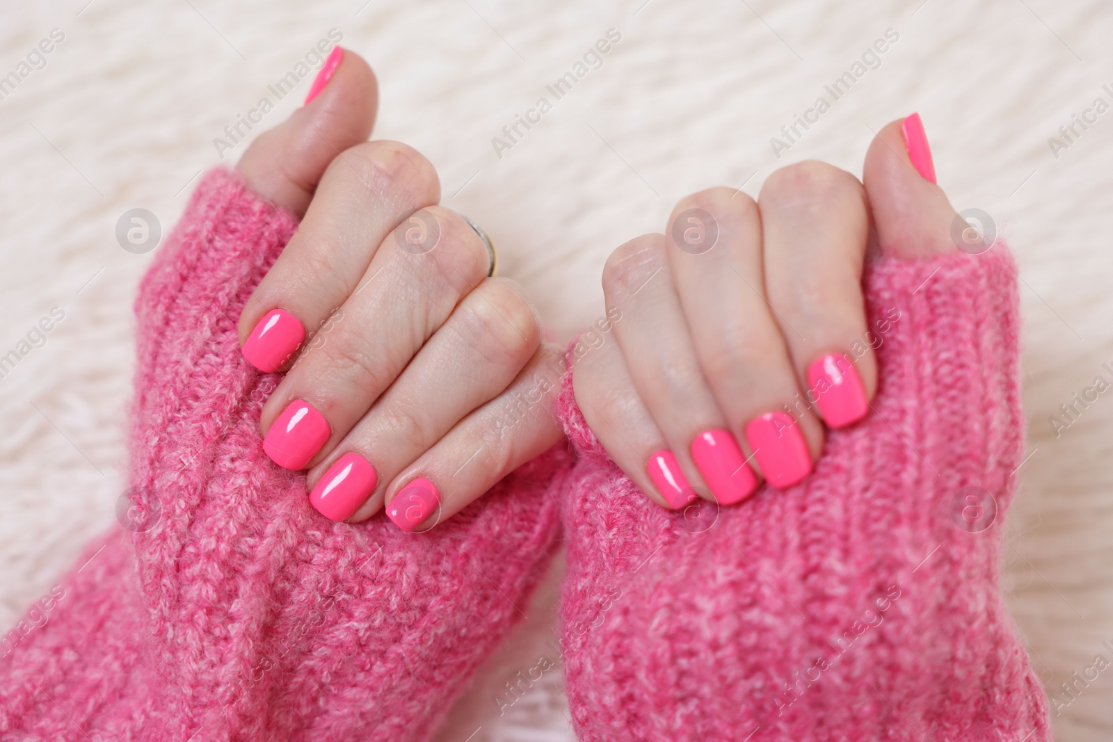 Photo of Woman showing her manicured hands with pink nail polish on faux fur mat, closeup