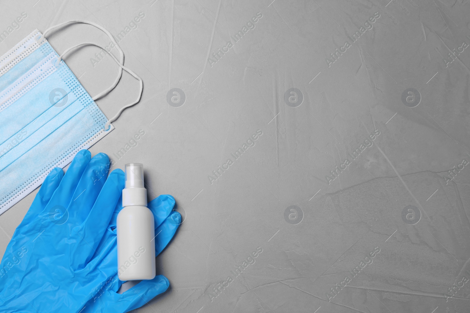 Photo of Protective masks, medical gloves and antiseptic on light grey stone background, flat lay with space for text