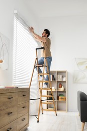 Man on wooden folding ladder installing blinds at home