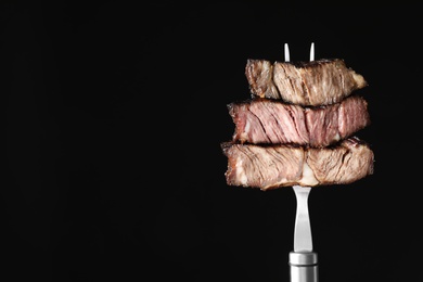 Fork with pieces of delicious barbecued meat on black background. Space for text