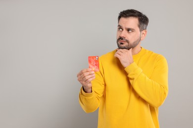 Photo of Confused man with credit card on grey background, space for text. Debt problem