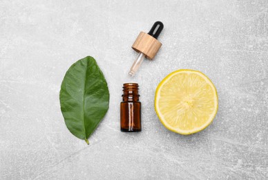 Photo of Bottle of essential oil with lemon slice and leaf on grey table, flat lay