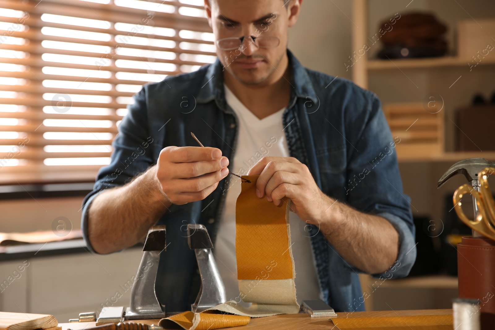 Photo of Man sewing piece of leather in workshop, focus on hands