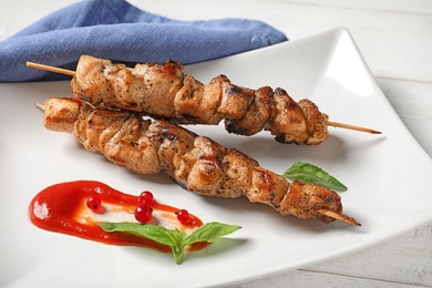 Photo of Plate with juicy shish kebab and sauce on table, closeup