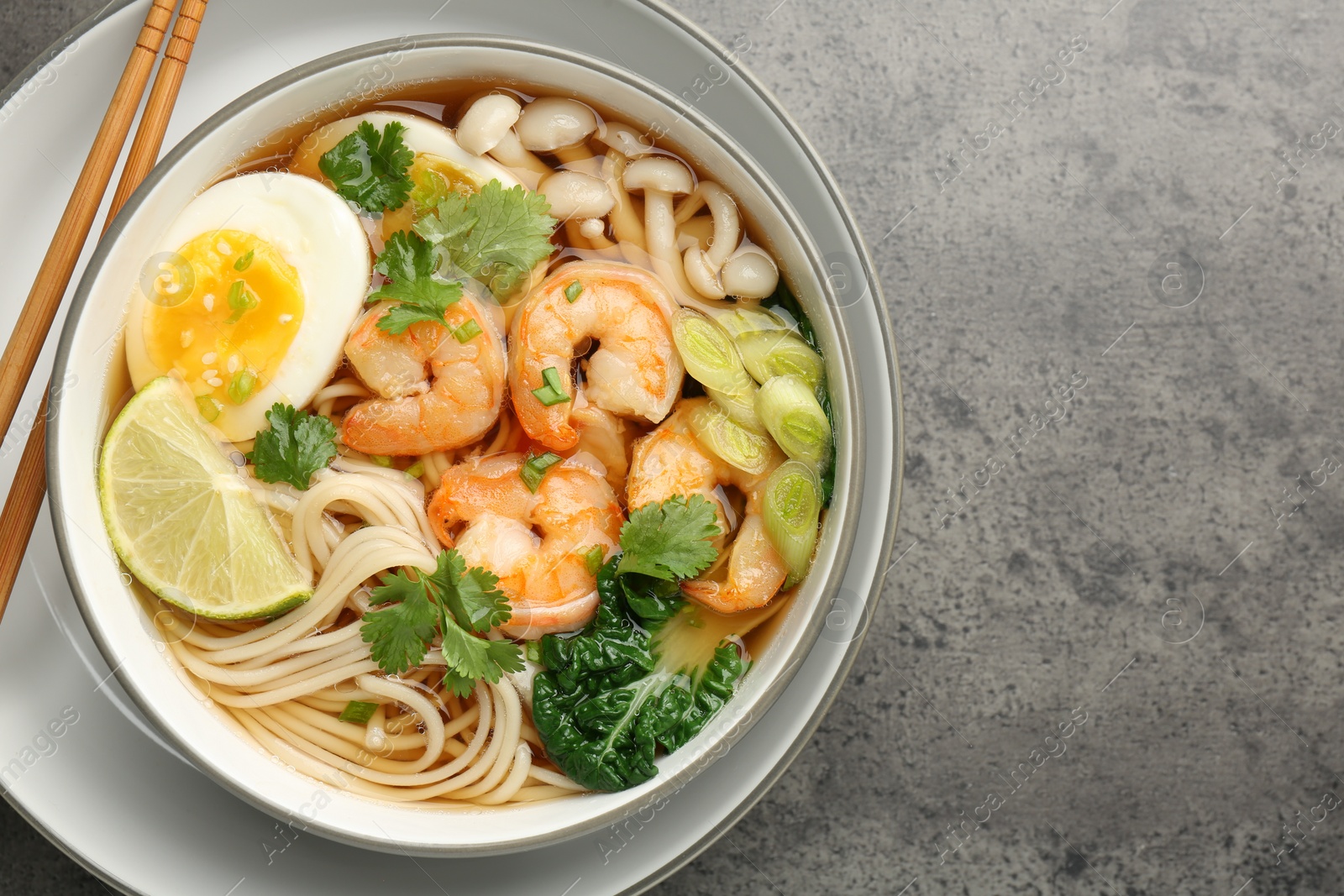 Photo of Delicious ramen with shrimps and chopsticks on grey table, top view with space for text. Noodle soup