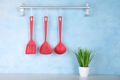 Rack with kitchen utensils hanging on light blue wall