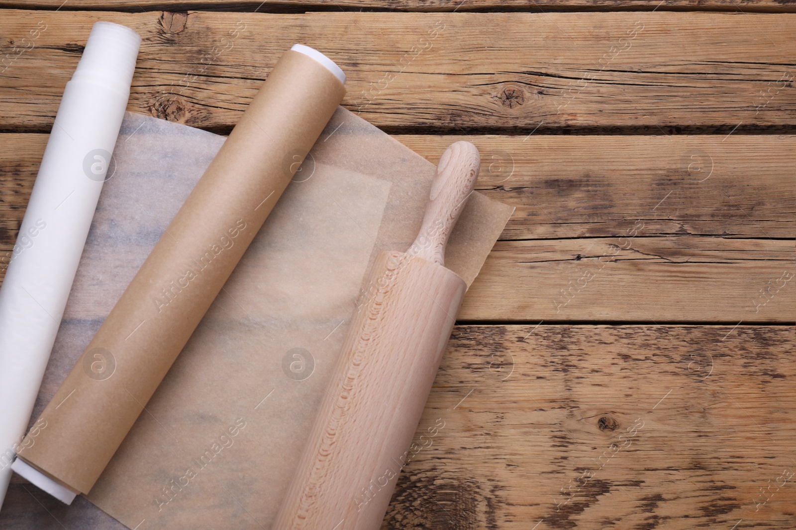 Photo of Rolls of baking parchment paper and rolling pin on wooden table, top view. Space for text