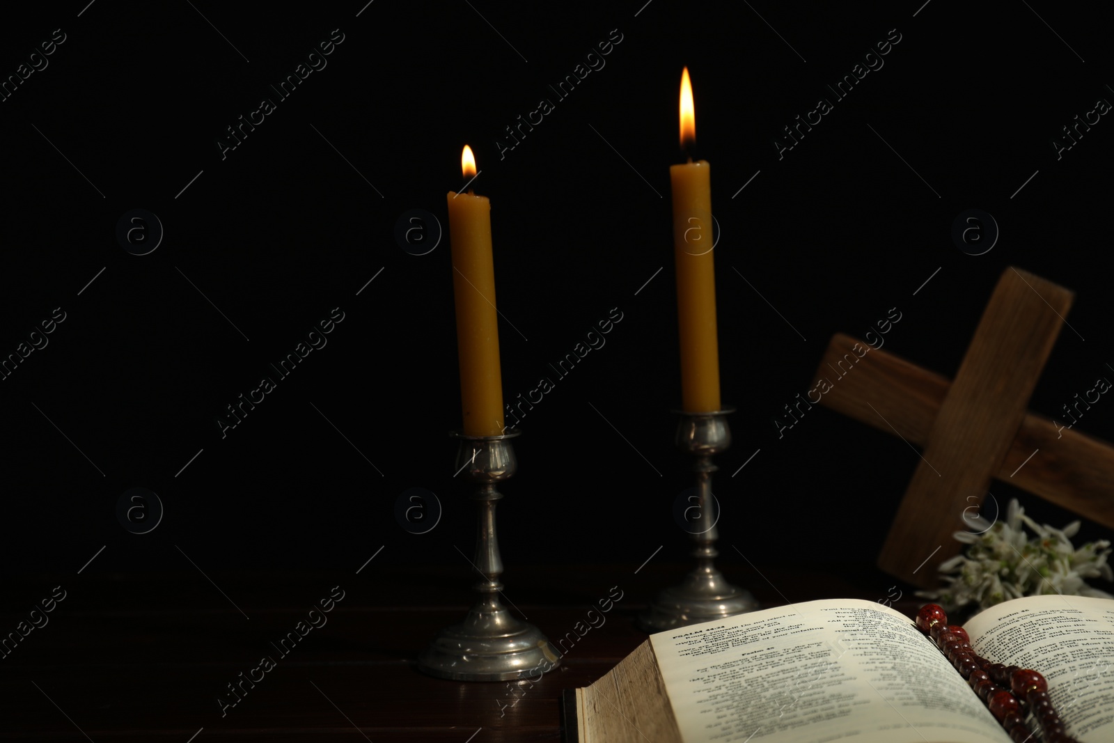 Photo of Church candles, Bible, cross and rosary beads on wooden table against black background, space for text