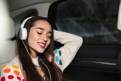 Photo of Beautiful young woman listening to music with headphones in car. Space for text