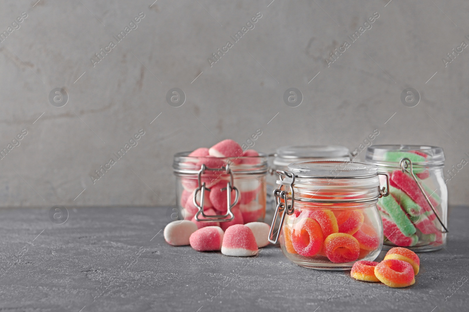 Photo of Glass jars with tasty jelly candies on grey table, space for text