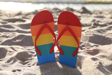 Photo of Stylish rainbow flip flops in sand on beach