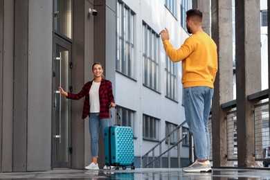 Photo of Long-distance relationship. Man waving to his girlfriend with suitcase near building outdoors